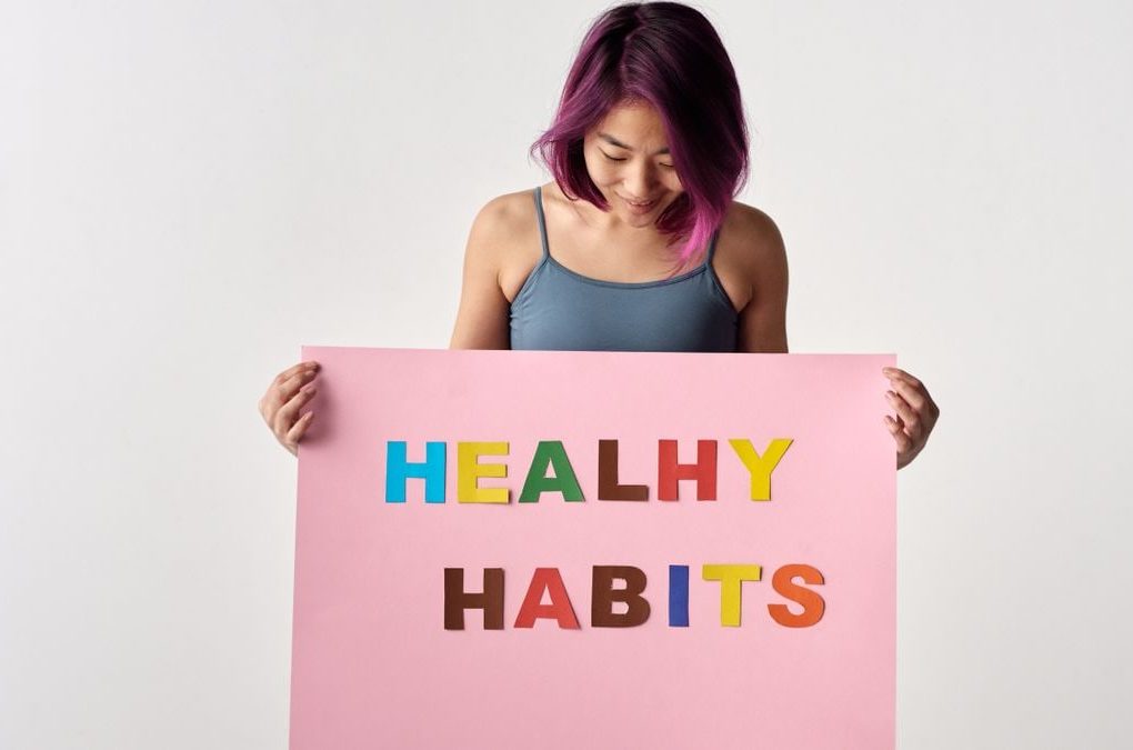 Asian woman holding a colorful 'Healthy Habits' sign in a studio setting, promoting wellness.