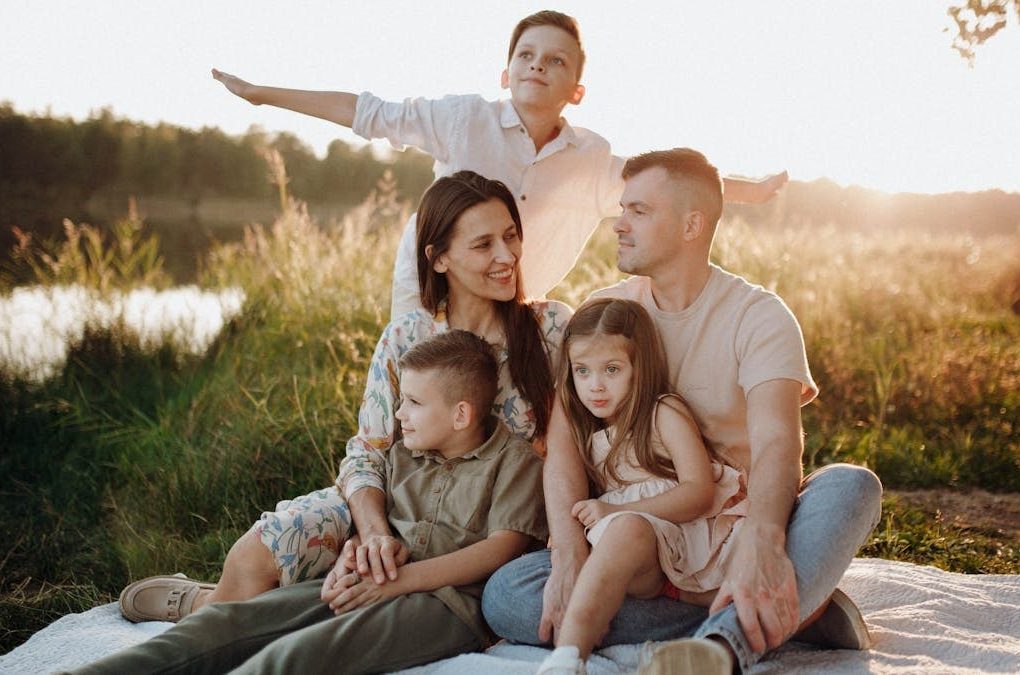 A family of five enjoying a serene picnic in a sunlit meadow during sunset.