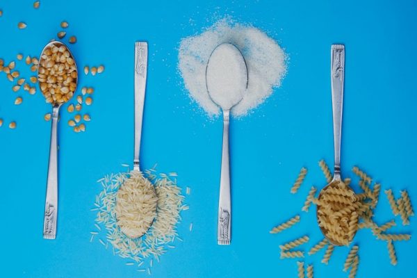 Four spoons with popcorn, rice, sugar, and pasta on a blue background. Perfect for food-related projects.